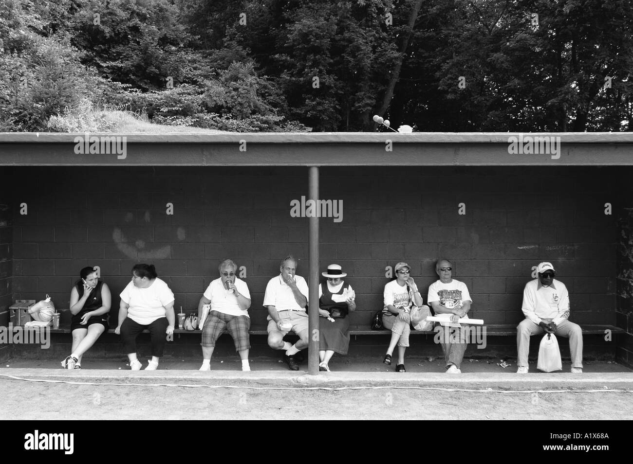 A row of people sitting in the shade on a baseball bench during a public festival in the summer in CT USA Stock Photo