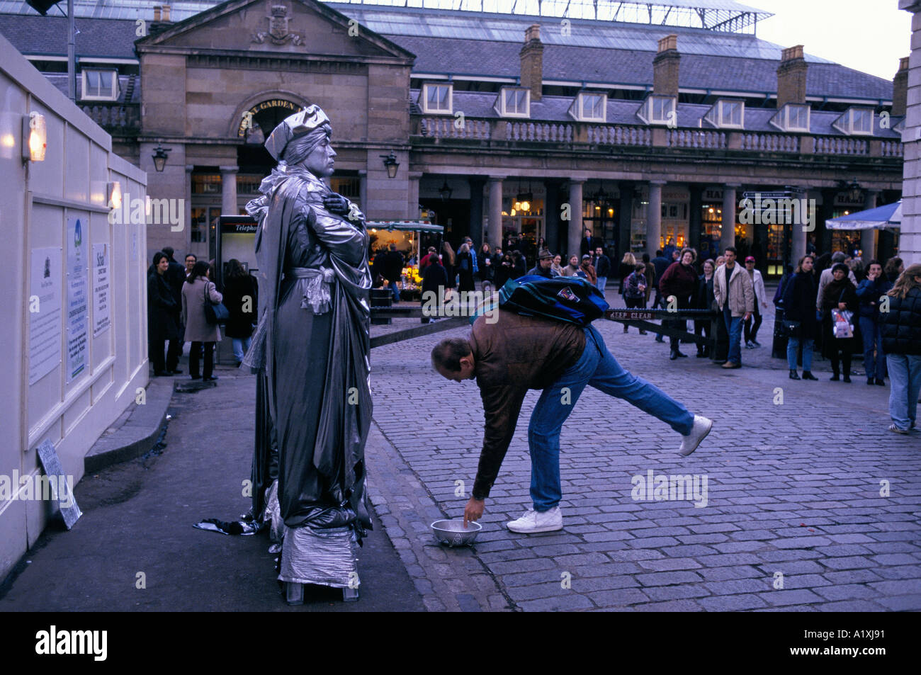 MEMBER OF THE CROWD BENDS OVER TO GIVE MONEY TO HUMAN STATUES