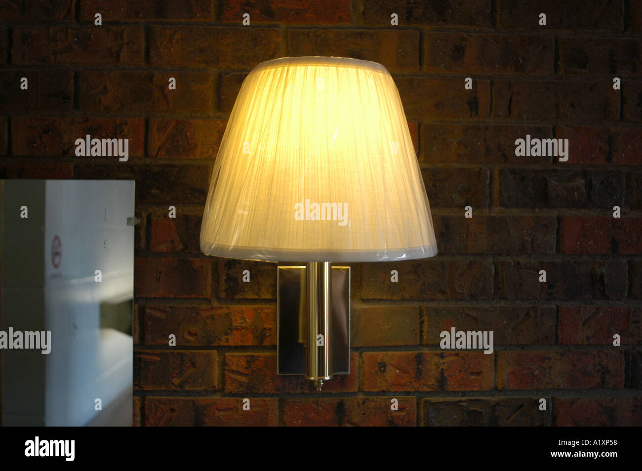 Plastic wrapping on a glowing lampshade on a light stuck onto a dark brick wall in a motel room Stock Photo