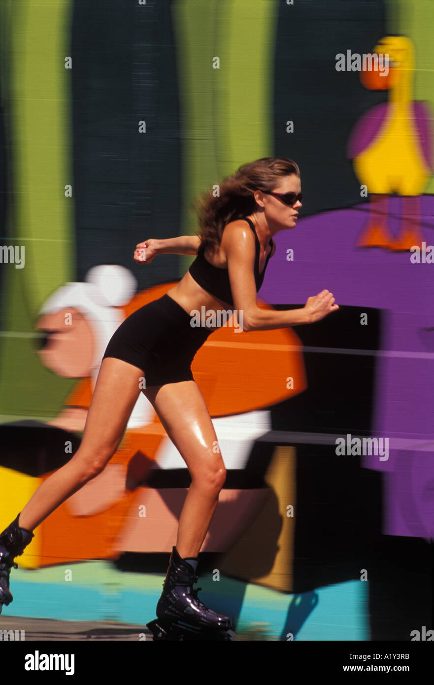 A woman rollerblades past a colorul wall mural on a sunny summer day Stock Photo