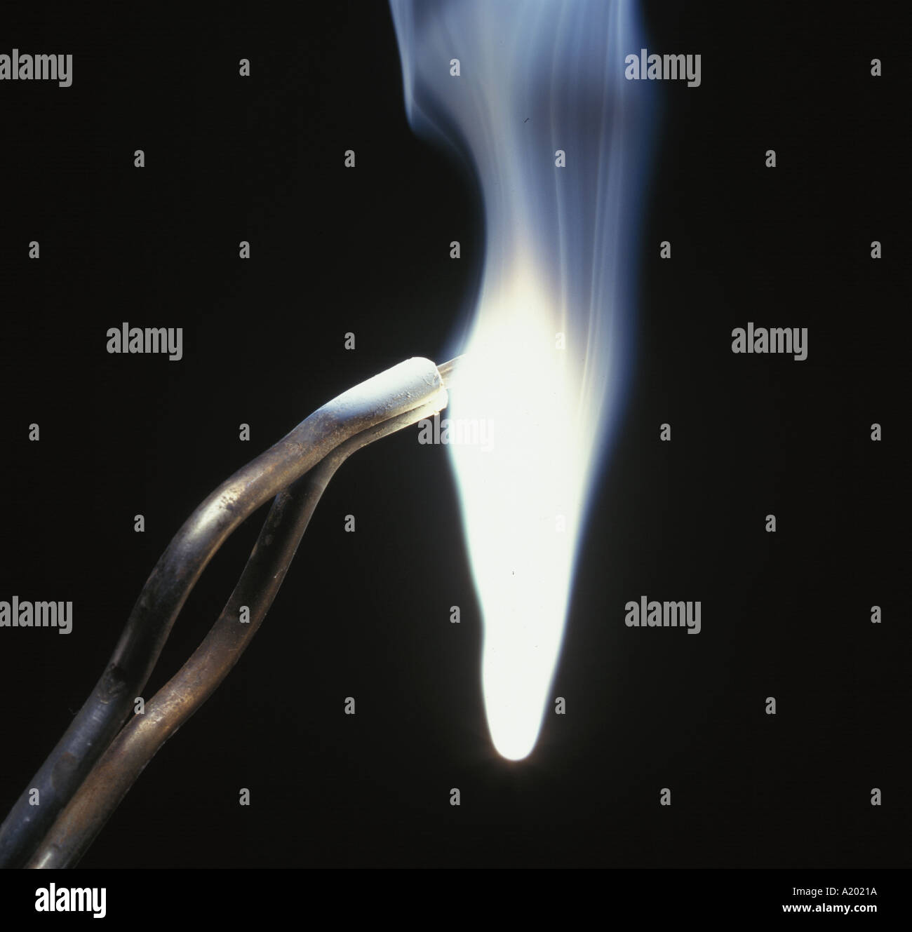 Magnesium (Mg) ribbon held by tongs burning extremely brightly in air with a brilliant white flame and smoke. Exothermic reaction. See also A20219 Stock Photo