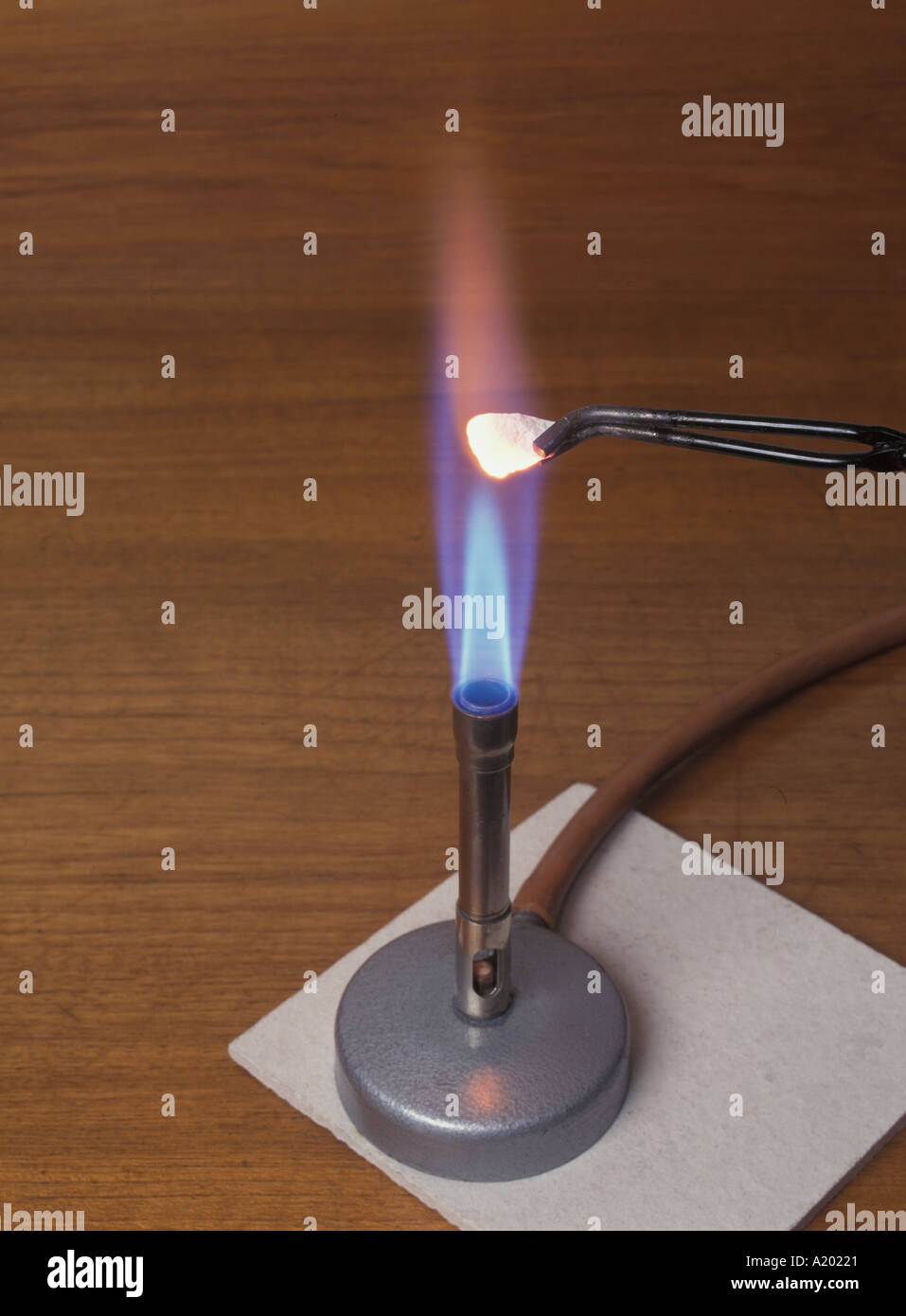 A piece of white marble being heated with a Bunsen burner producing a blue flame on a heatproof mat. This is a common school chemistry experiment Stock Photo