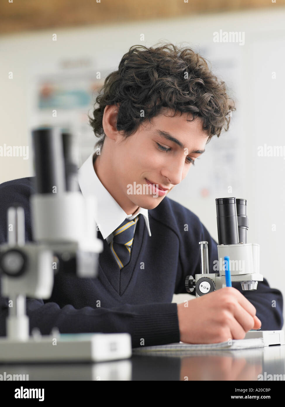 High school student using microscope and taking notes in classroom ...