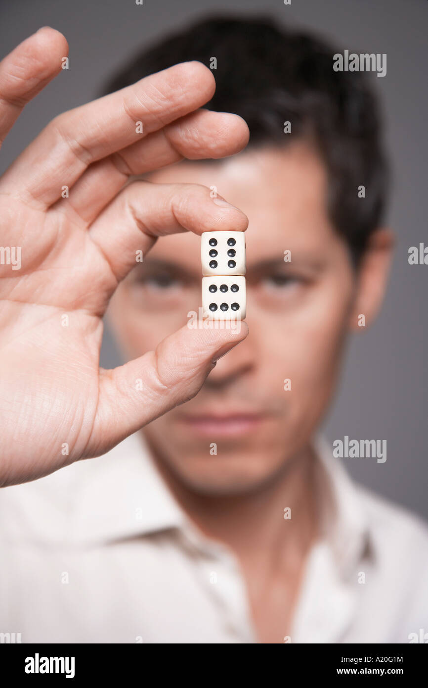 Man holding dice between finger and thumb, focus on foreground Stock Photo