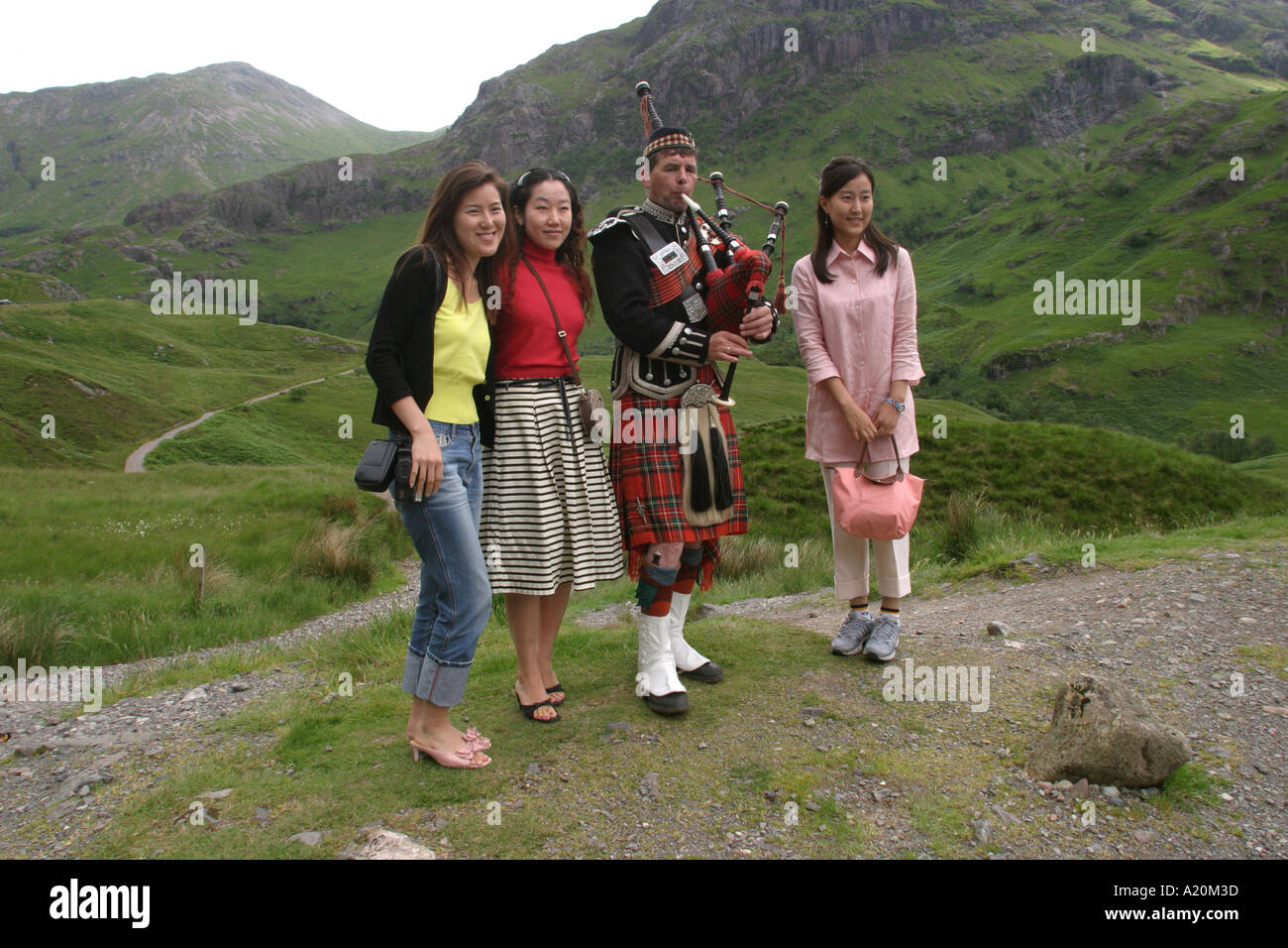 Korean tourists pose for photos with a bagpiper, Glencoe, Scotland Stock Photo