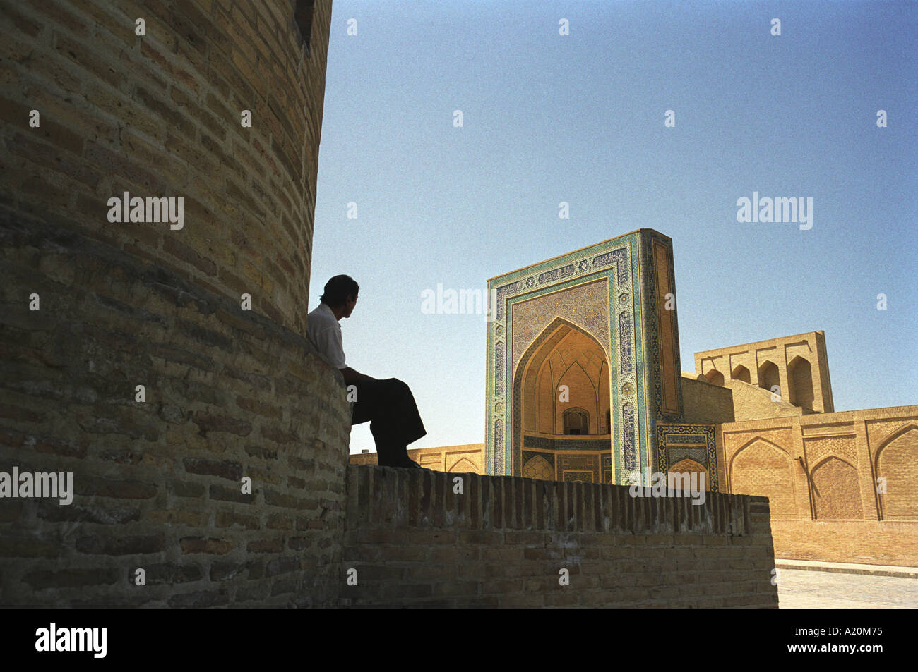 Sellers of carpets and tourist souvenirs sit in the shade outside the Kalan Mosque and Medressa, Bukhara, Uzbekistan Stock Photo