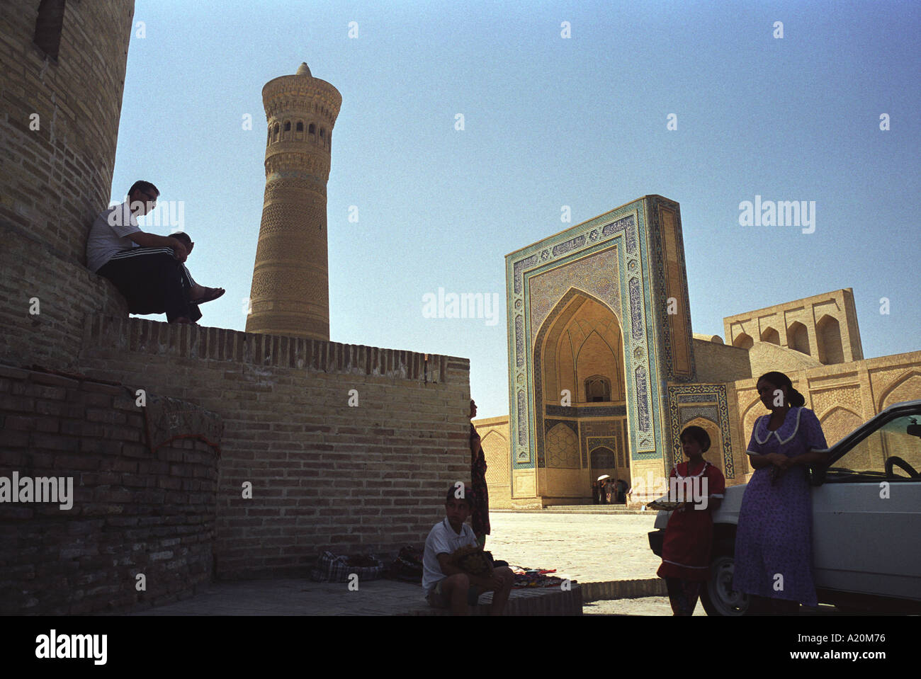 Sellers of carpets and tourist souvenirs sit in the shade outside the Kalan Mosque and Medressa, Bukhara, Uzbekistan Stock Photo