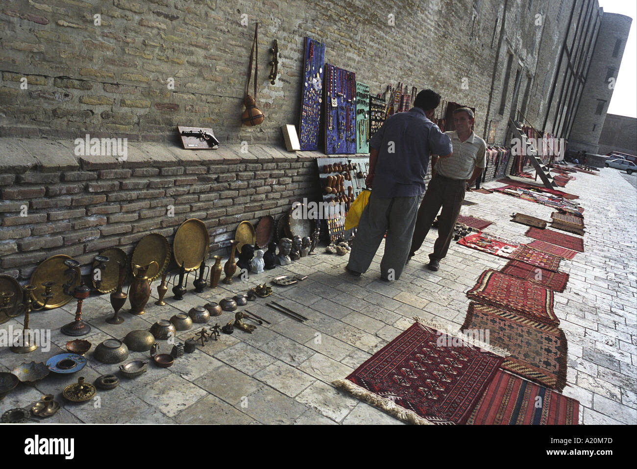 Sellers of carpets and tourist souvenirs in the shade outside the Kalan Mosque and Medressa, Bukhara, Uzbekistan Stock Photo