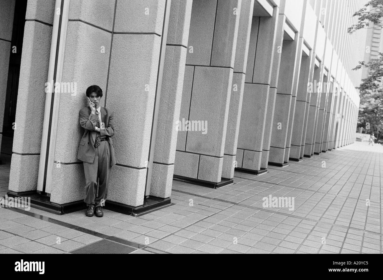 Sheltering against a building in Nishi Shinjuku an office worker uses his mobile telephone Stock Photo