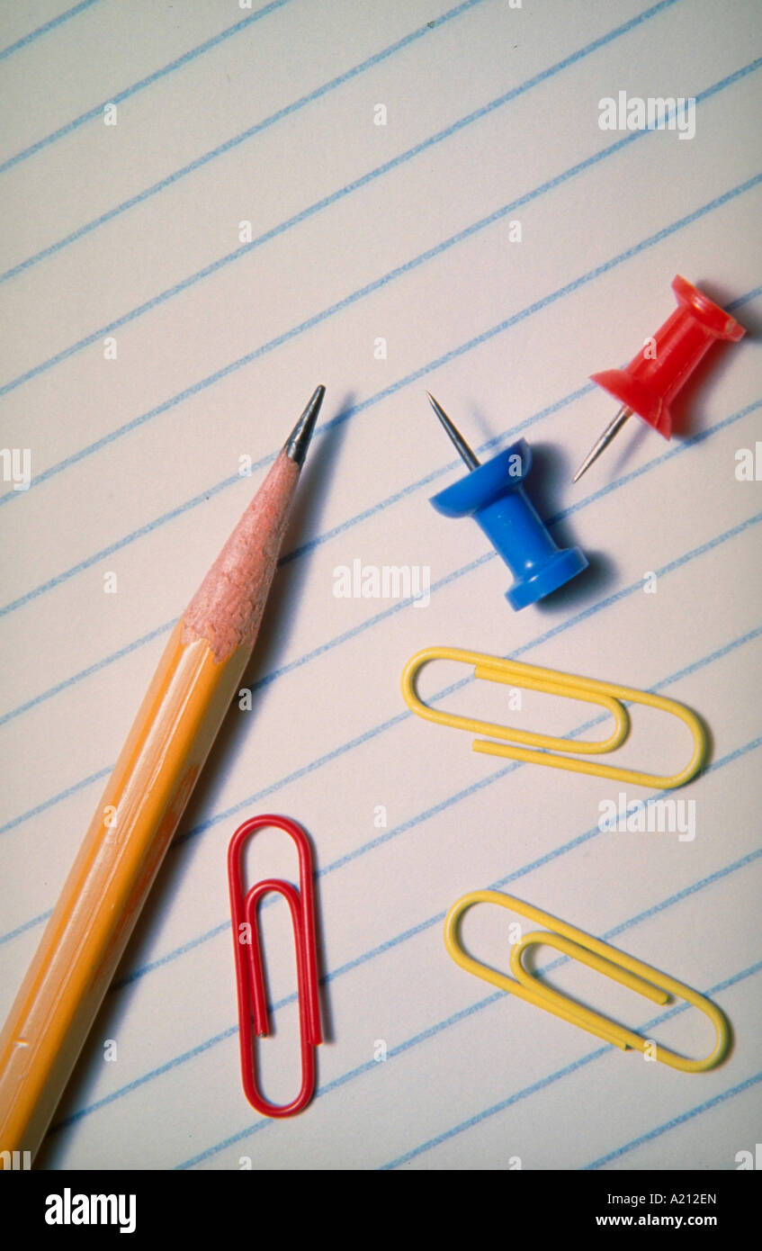 Pencil paper clips and thumbtacks laying on a piece of lined notebook ...