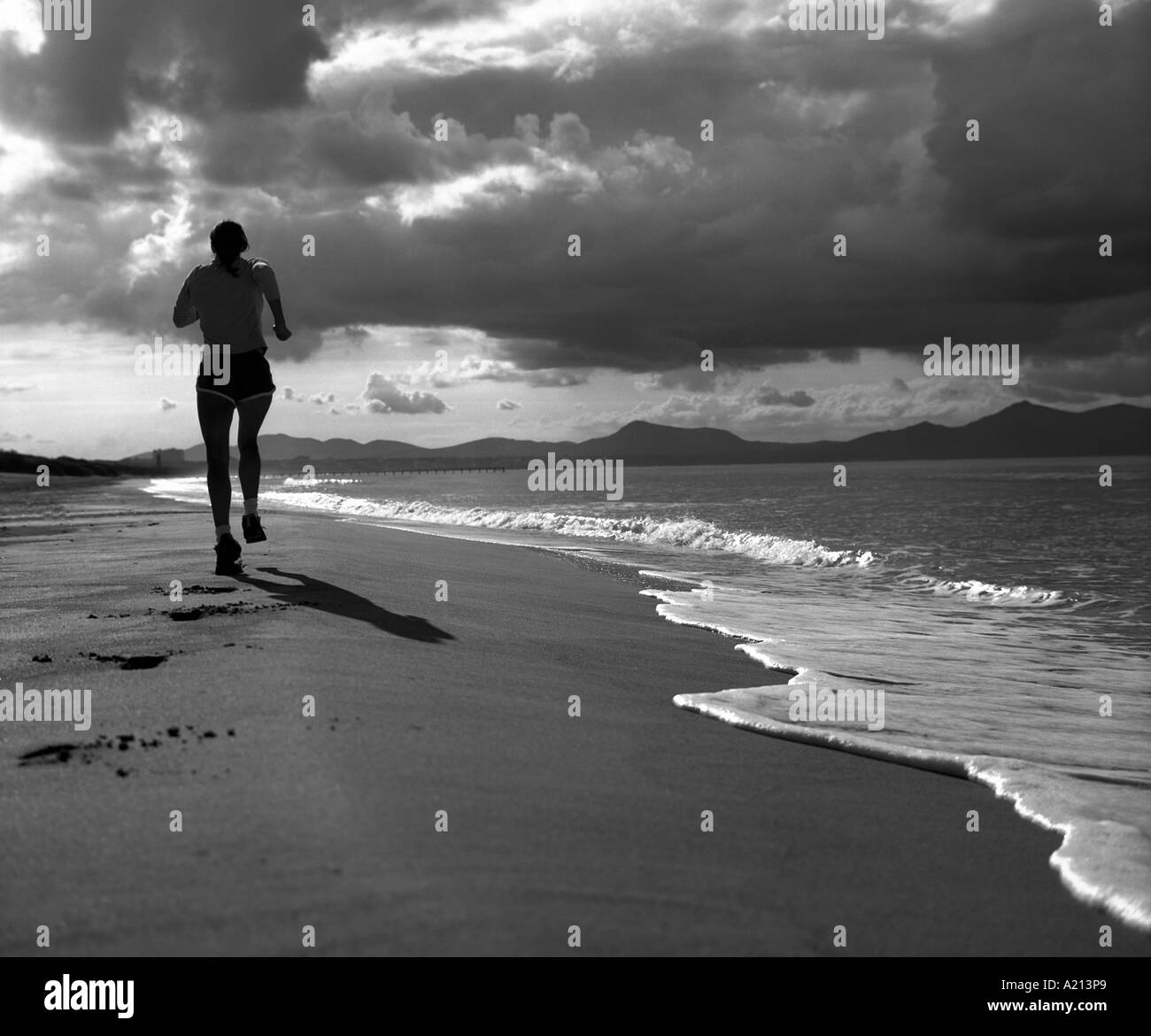 lone individual exercising on a beach in evening sunlight offering concepts of health and good living in black and white Stock Photo
