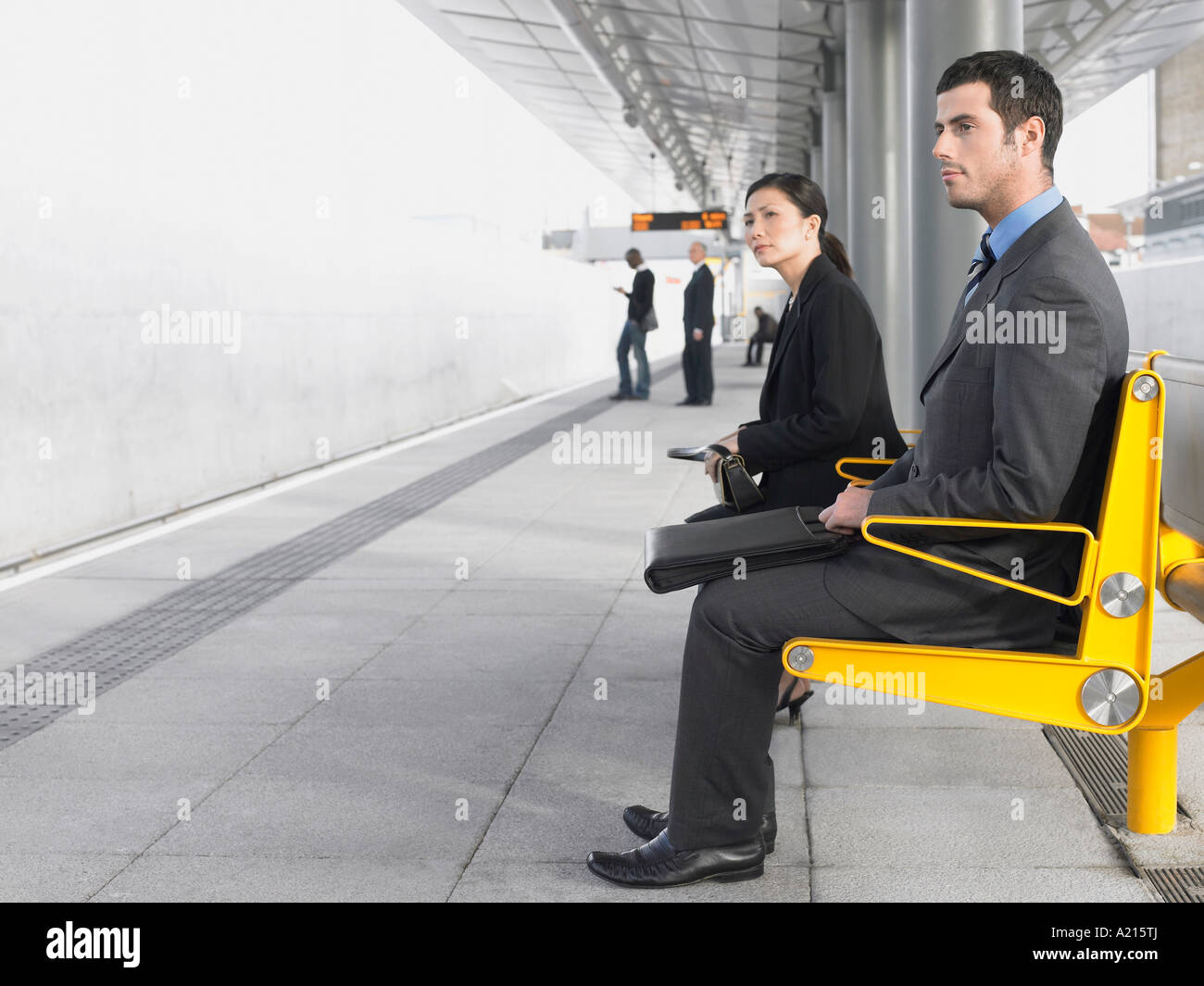 Businesspeople sitting on benches, Waiting at Train Station, side view Stock Photo