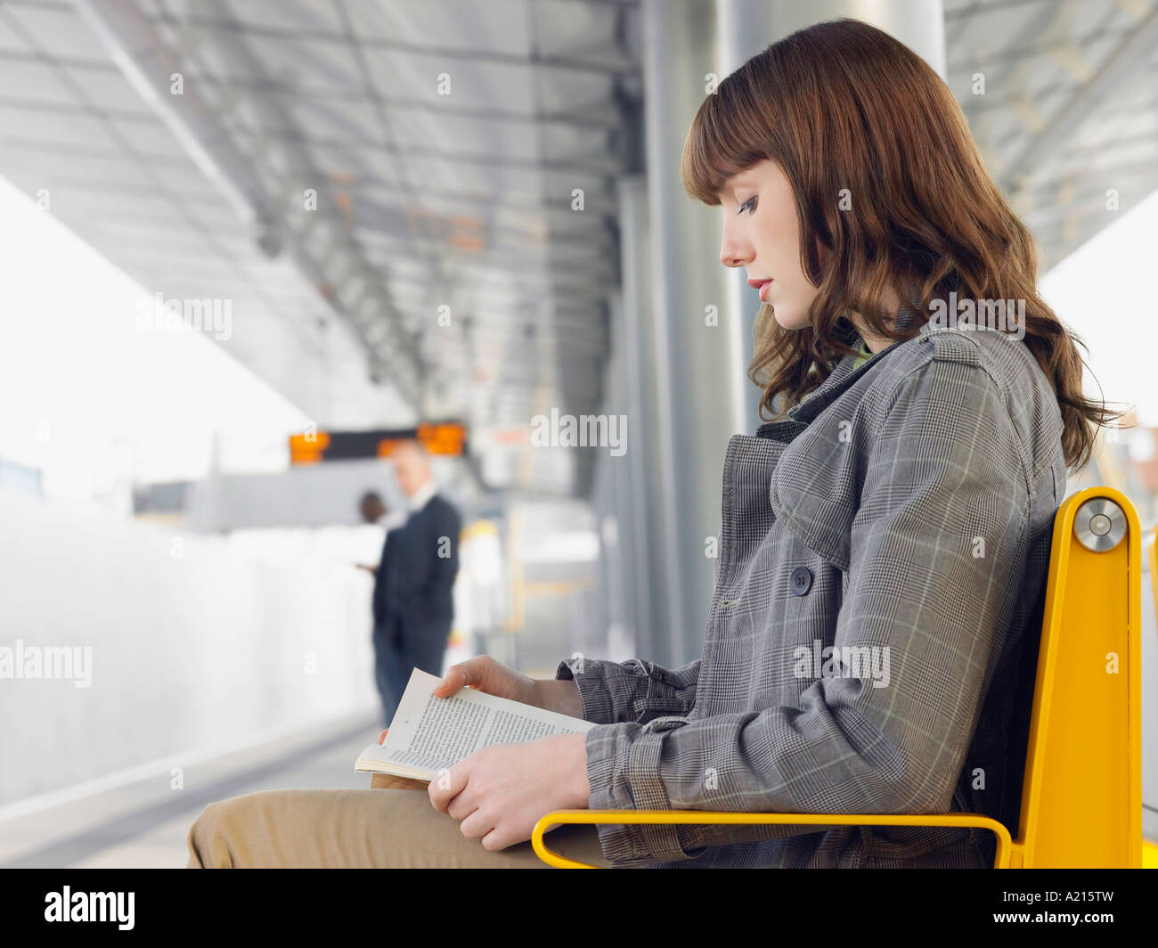 Businesswoman sitting on bench, reading a book at Train Station, side view Stock Photo