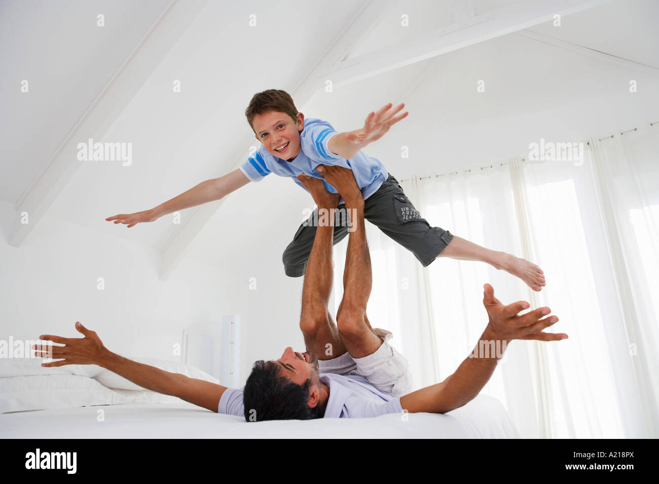 Son balancing on father's legs on bed in bedroom Stock Photo
