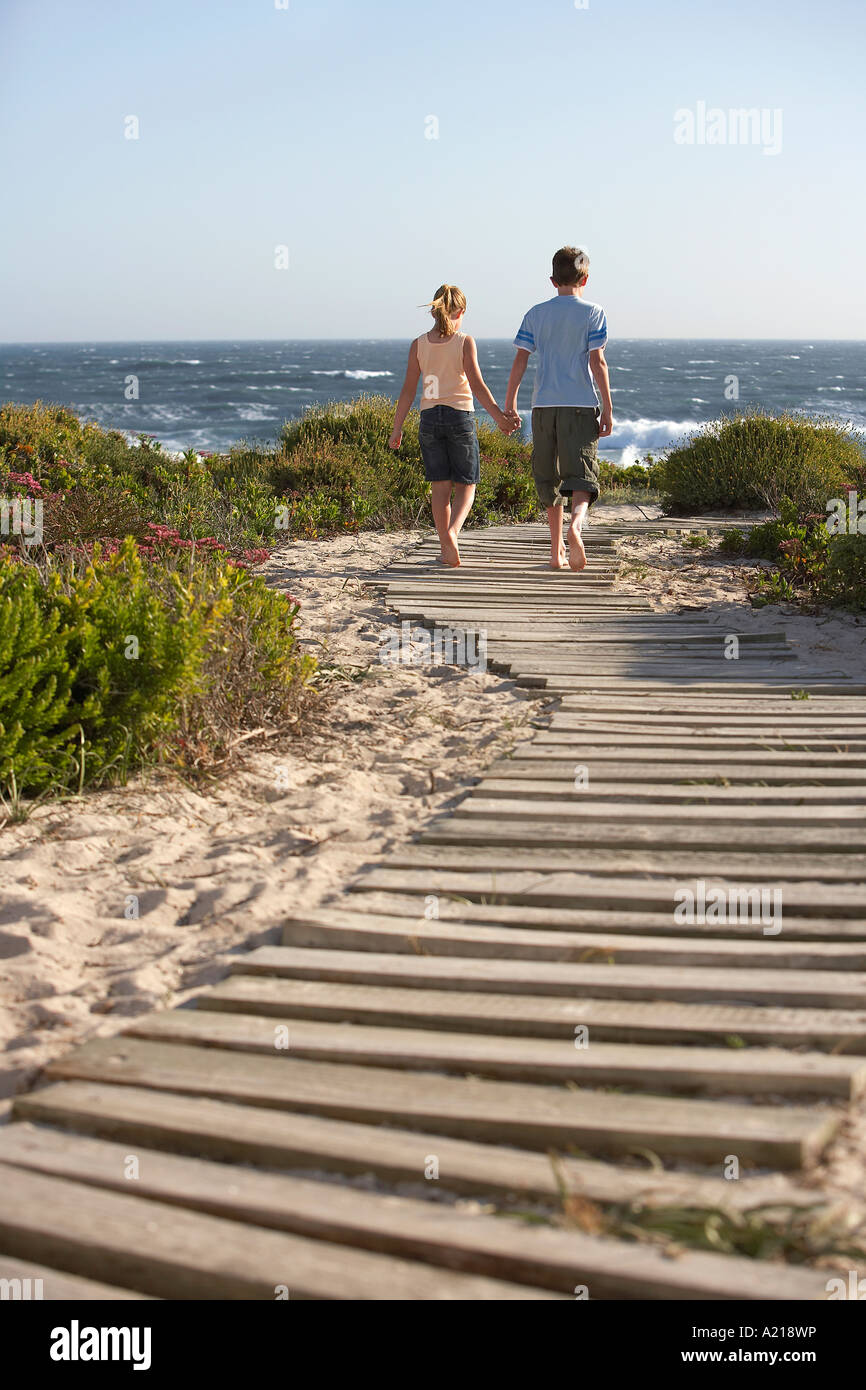 Boy and girl walking hand in hand, along boardwalk toward sea, back ...