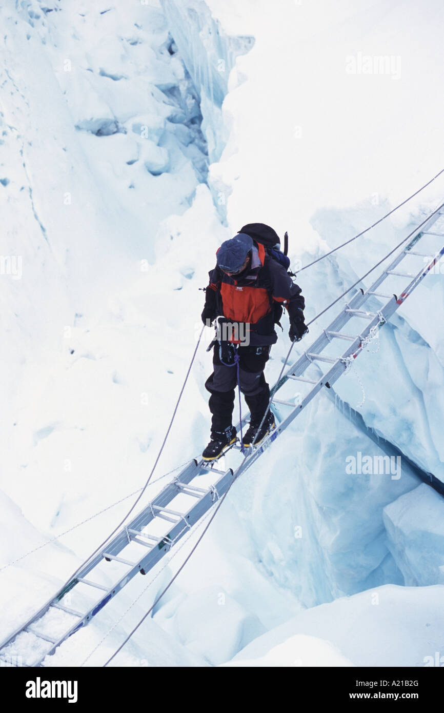 A climber on Mount Everest crossing a crevasse on a ladder in the Khumbu icefall in Nepal Stock Photo