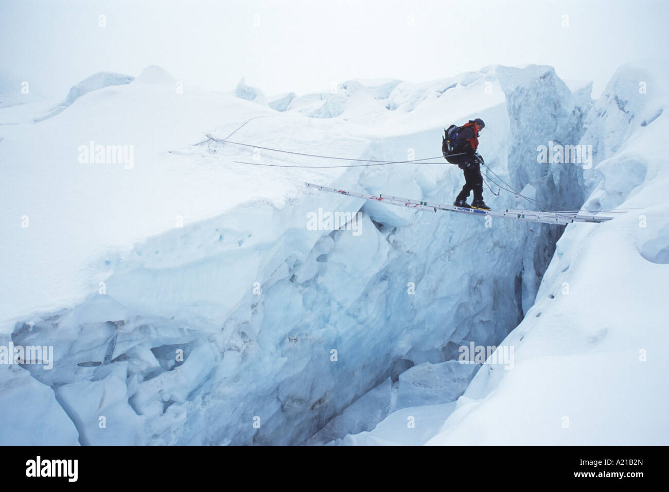 A climber on Mount Everest crossing a crevasse on a ladder in the Stock