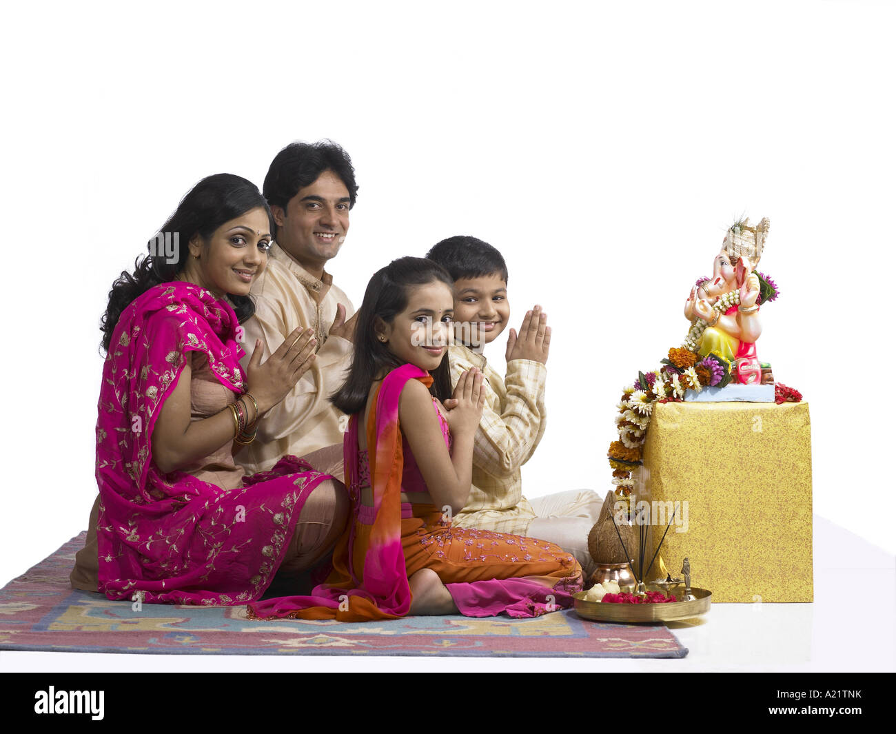 South Asian Indian family with father mother son and daughter praying to lord Ganesha smiling at camera wearing dress kurta Stock Photo