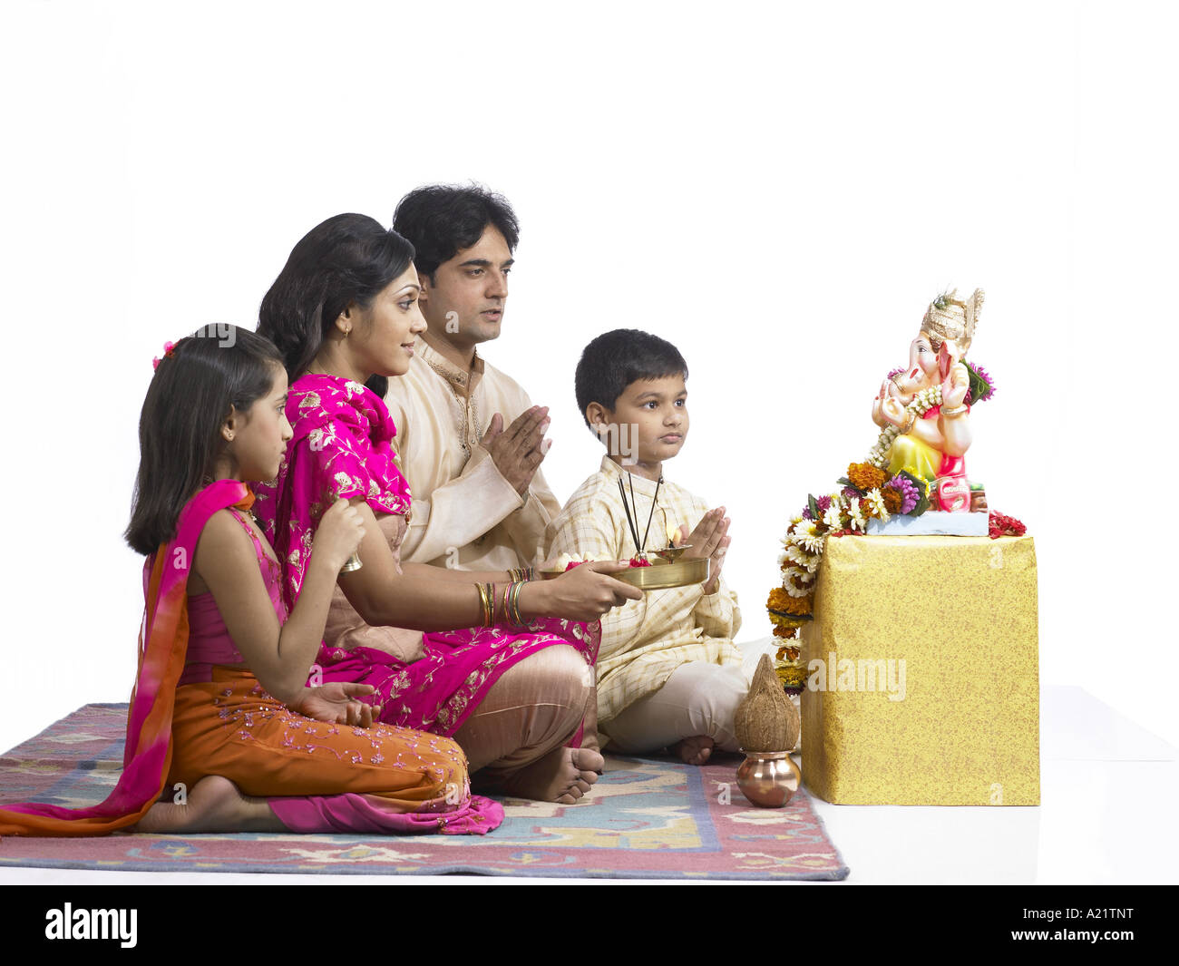 South Asian Indian family with father mother son and daughter sitting praying to lord Ganesha wearing traditional dress kurta Stock Photo
