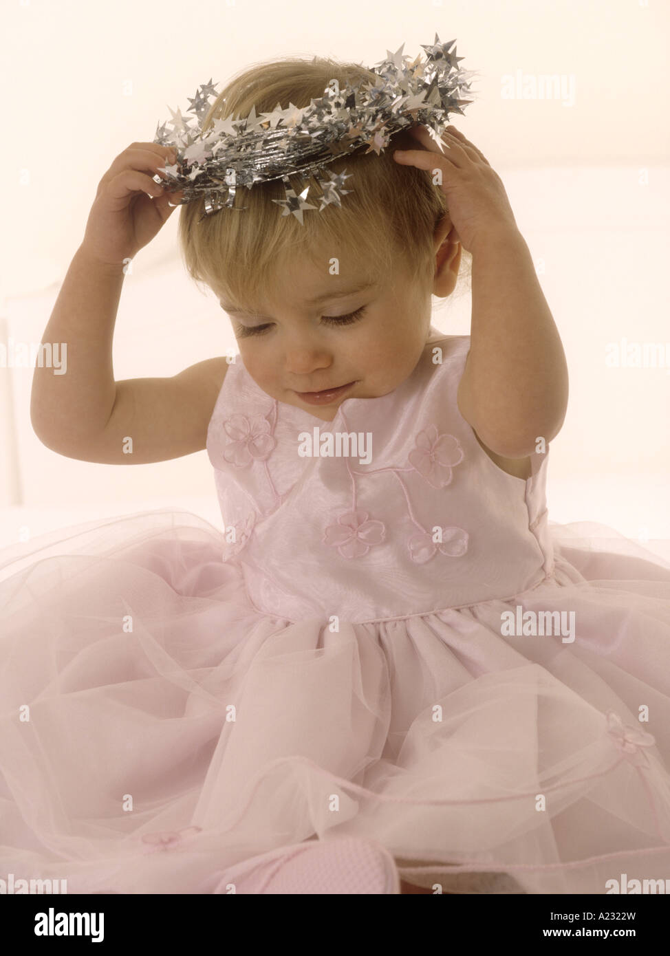 Toddler wearing a pink party dress looking at a tinsel halo Stock Photo