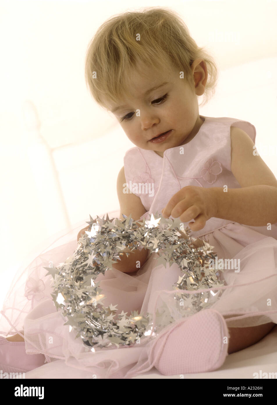 Toddler wearing a pink party dress looking at a tinsel halo Stock Photo