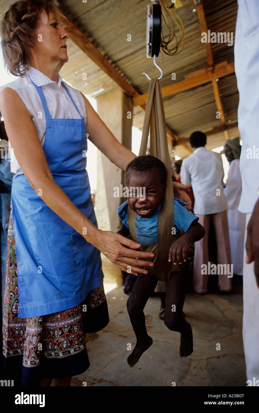 FAMINE IN SUDAN 1985 REFUGEE CAMP AT EL FASHER DARFUR REGION RED CROSS NURSE WEIGHS CHILD Stock Photo