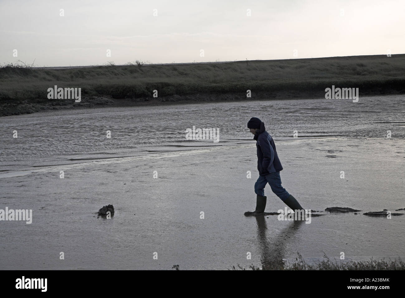 Teenage boy walking through muddy bed of River Ore tributary, Suffolk, England Stock Photo