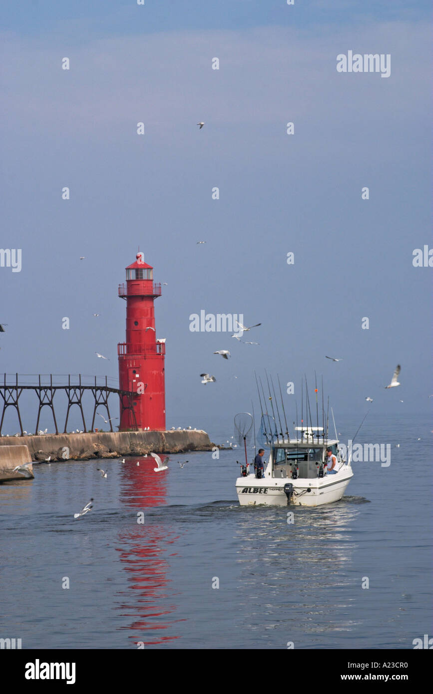 A small boat passing by a red light house in Alogoma Wisconsin Stock Photo