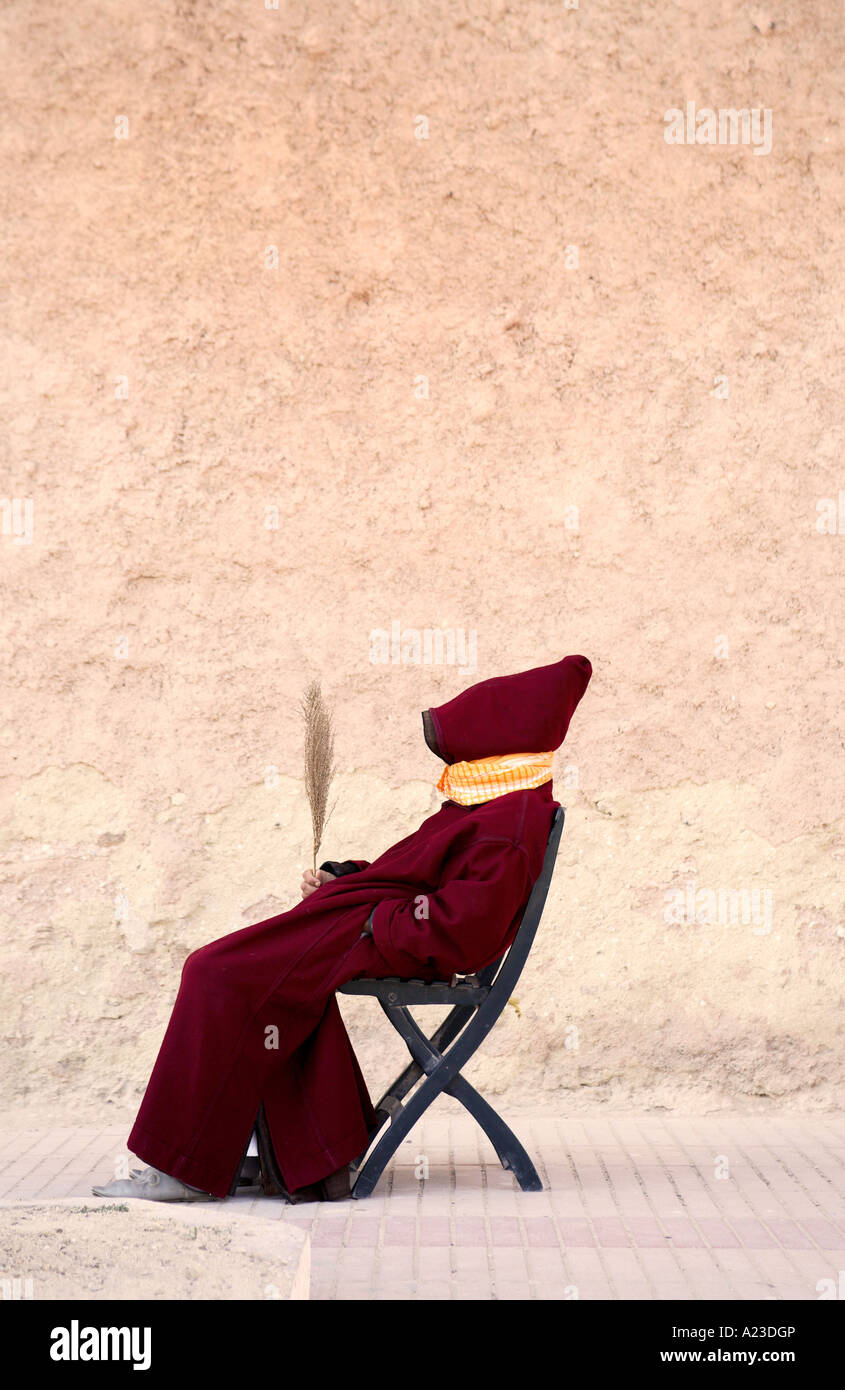 a moroccan man wearing a traditional jellaba sits in the street beside the old medina wall Stock Photo