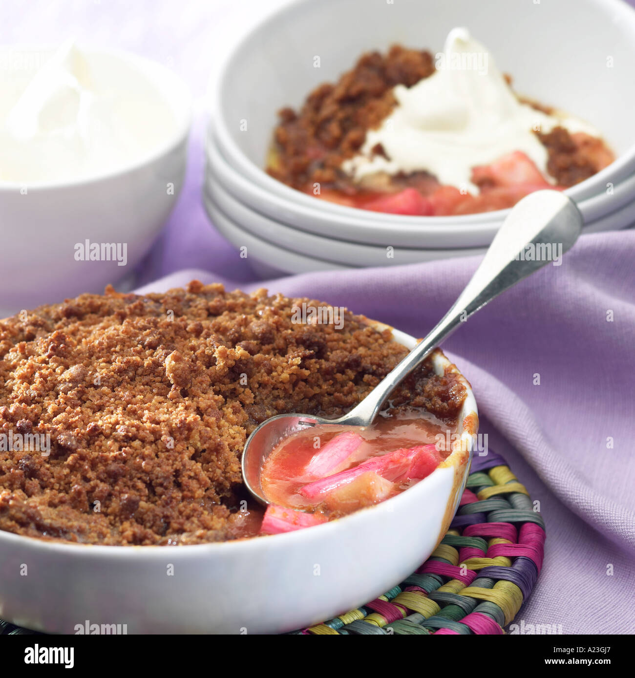 Rhubarb Crumble, whole with portion in b/g with cream Stock Photo