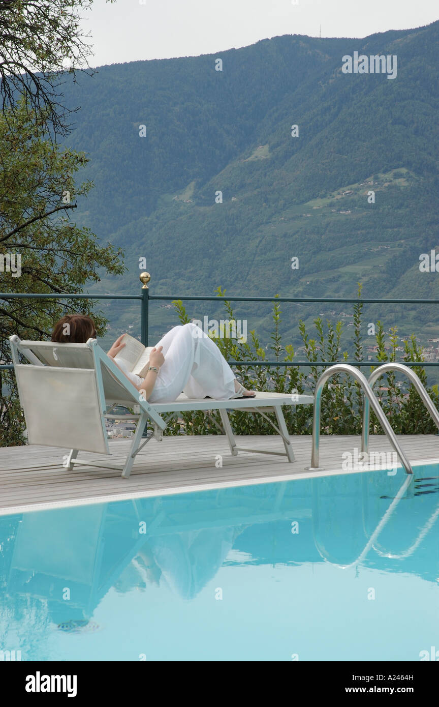 Young woman sitting beside the swimming pool reading a book Stock Photo ...