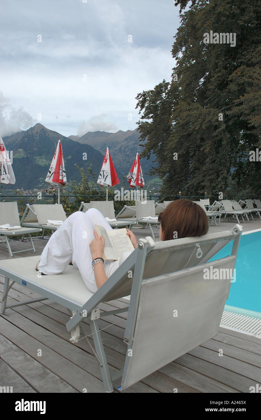 Young woman sitting beside the swimming pool reading a book Stock Photo ...