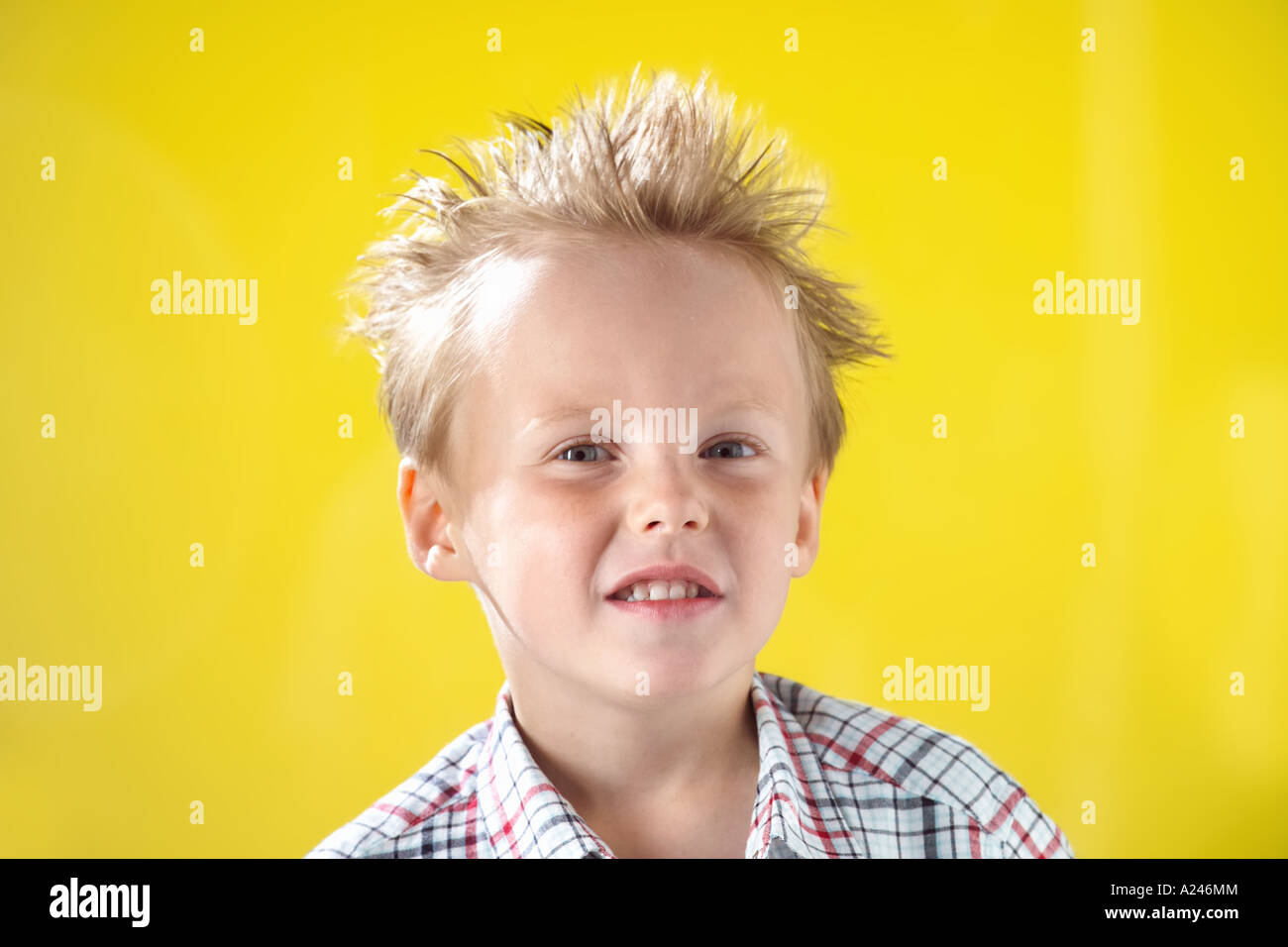 Blonde Boy aged 5-7 years against yellow studio background pulling funny faces while having his hair blow dried. Stock Photo