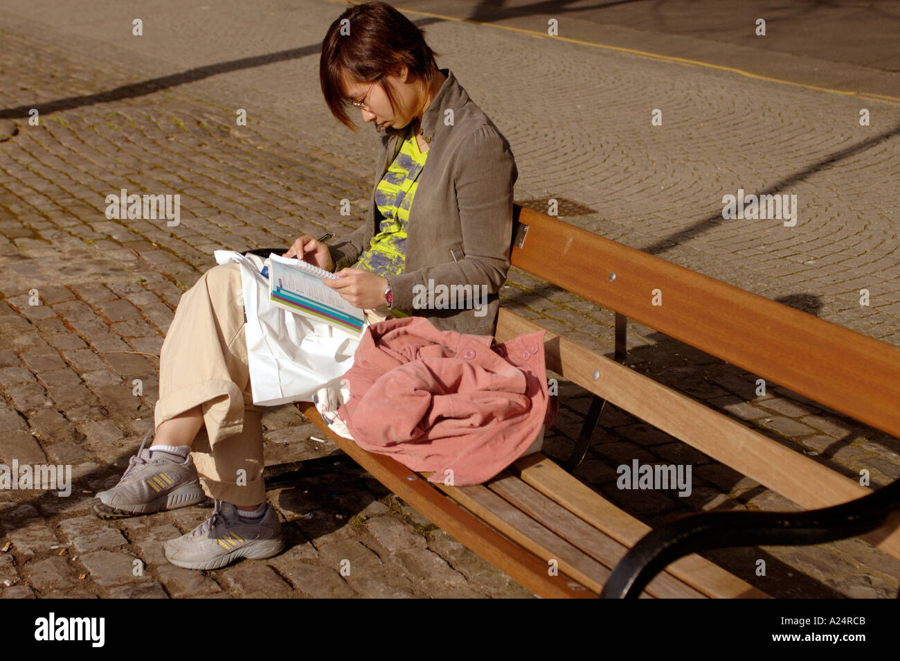 Woman sitting by herself on park bench reading with her head down Stock Photo