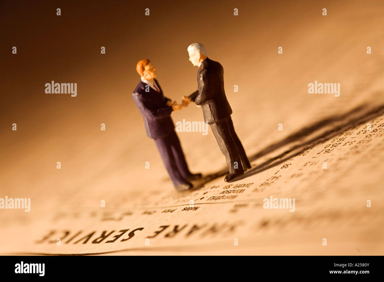 Miniature businessmen shake hands standing on financial newspaper Stock Photo