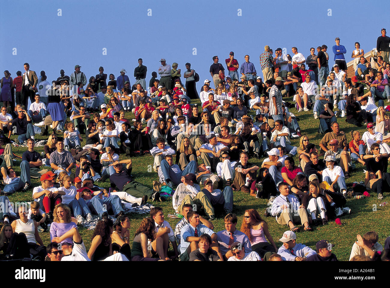 CROWD OF PEOPLE SITTING OUTSIDE ON GRASS SLOPE Stock Photo