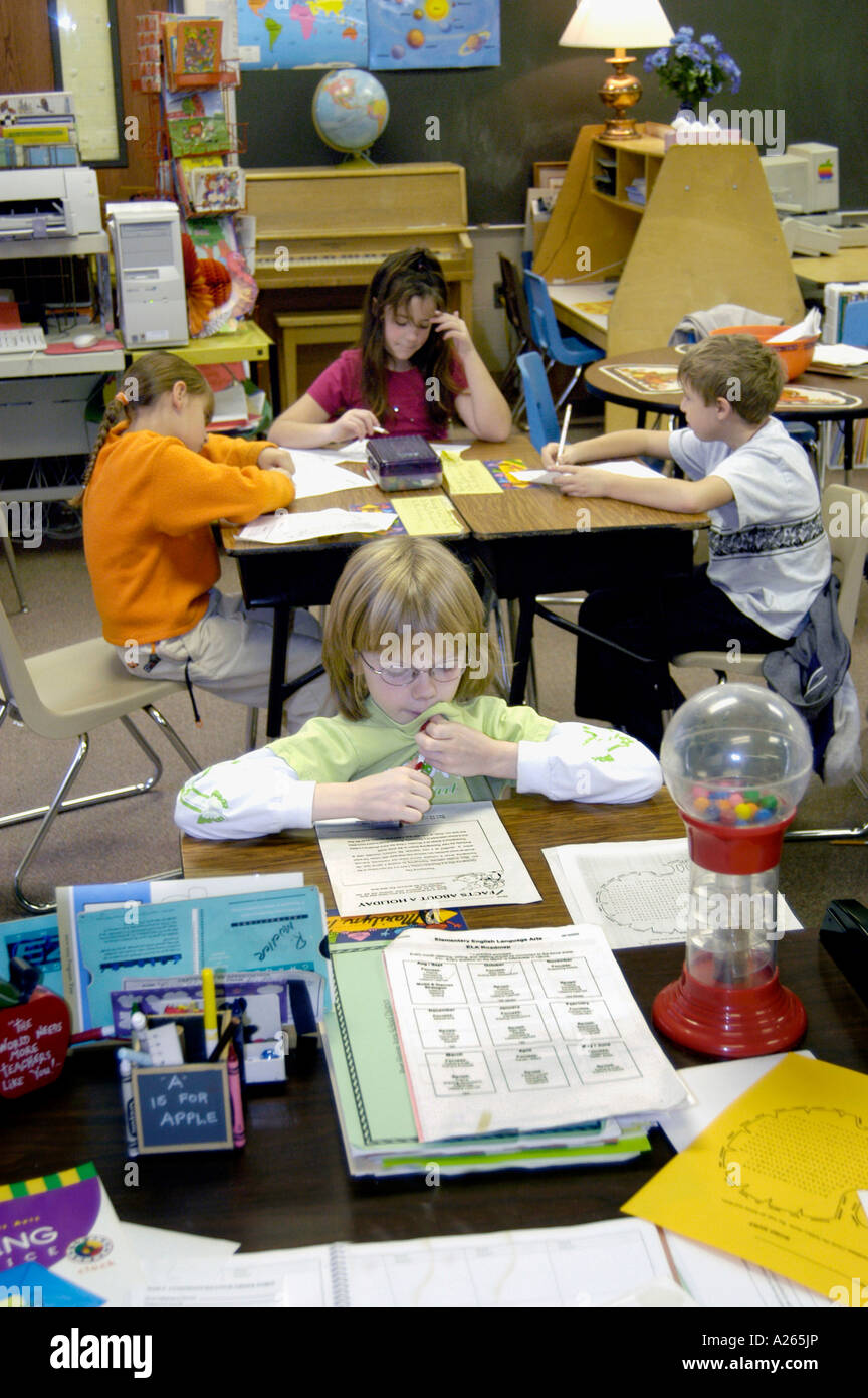 3rd grade elementary student isolated working alone away from a group of 3 students Stock Photo