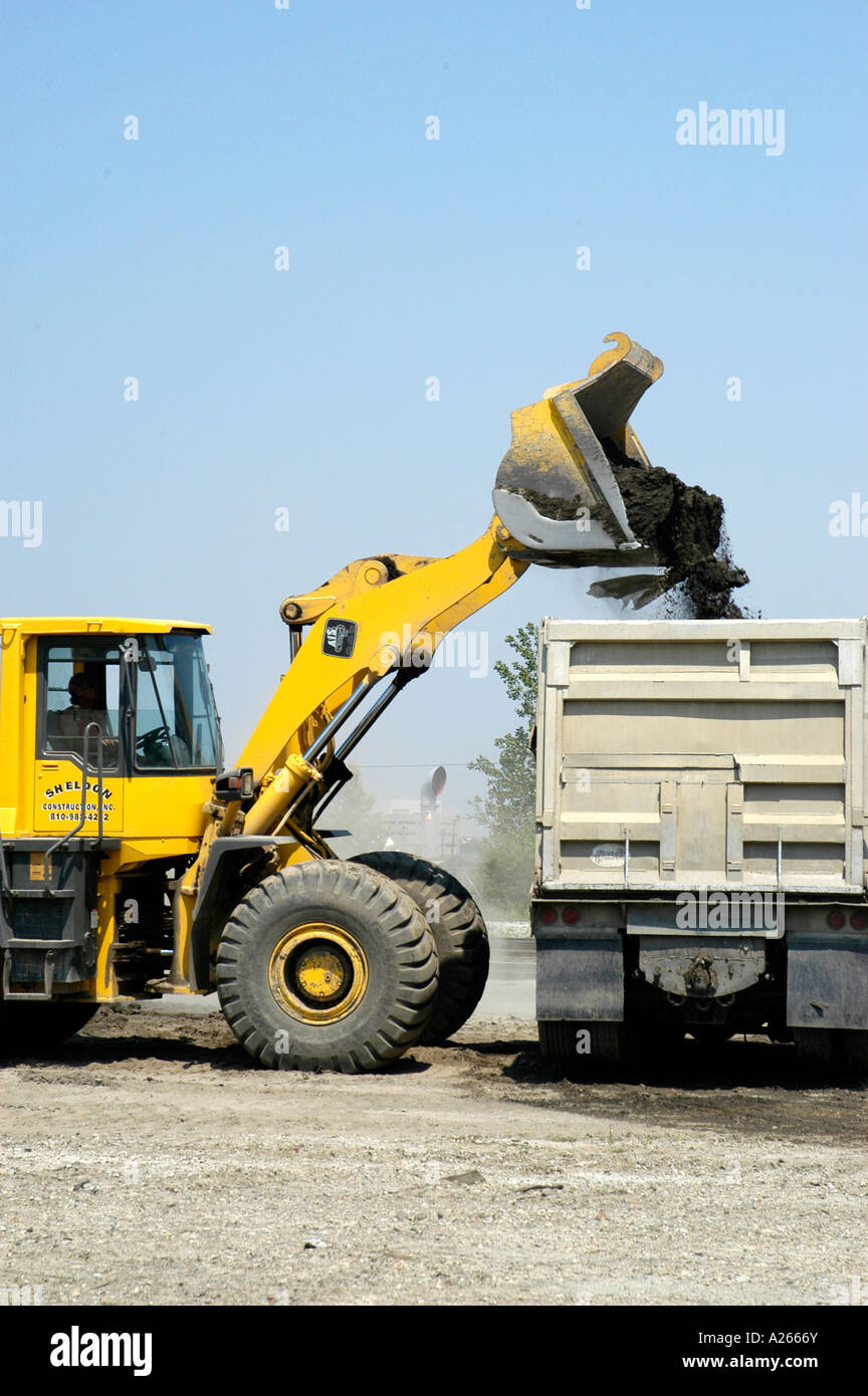 Large excavator fills a dump truck with black dirt Stock Photo