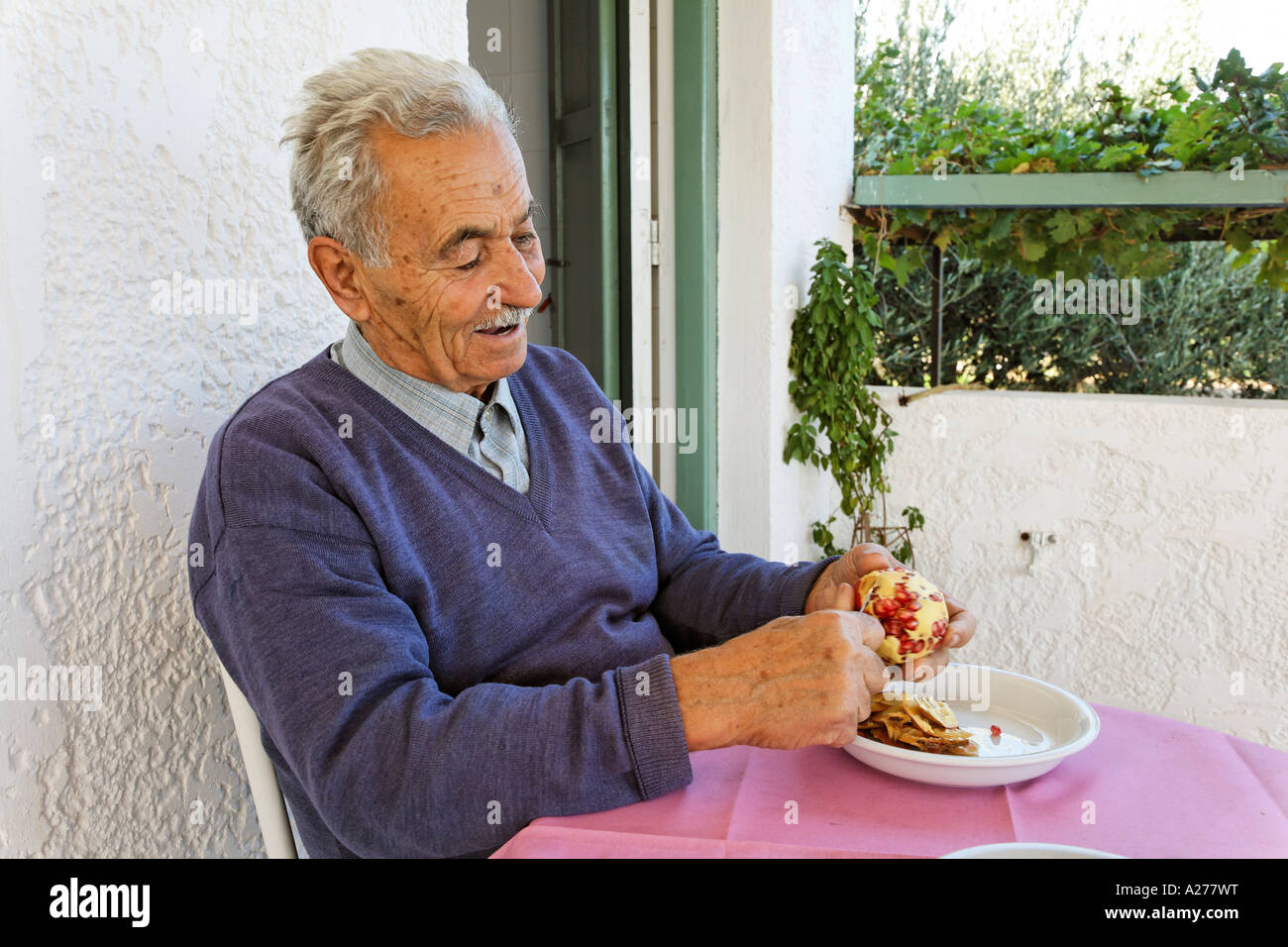 Old man peeling pomegranate, Palekastro, Crete, Greece Stock Photo