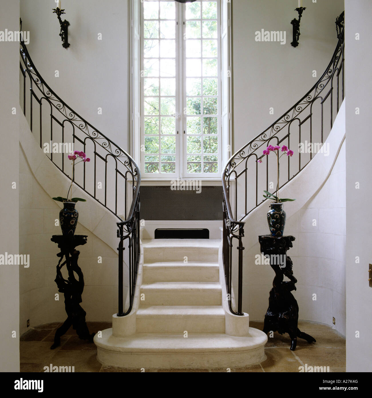 Stone grand staircase with wrought iron banister and large paned window Stock Photo