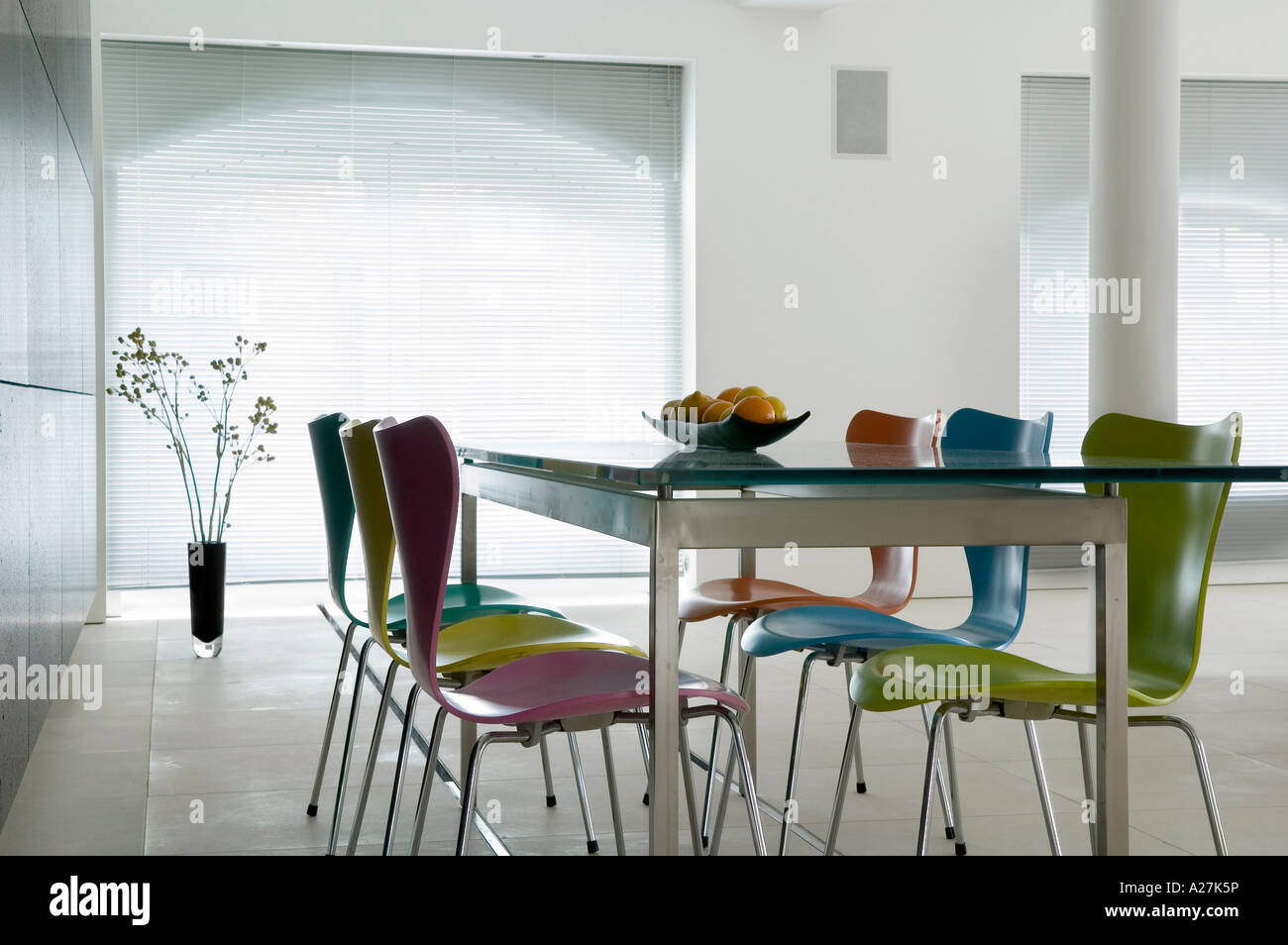 Glass topped table with coloured butterfly chairs in minimalist warehouse conversion Stock Photo