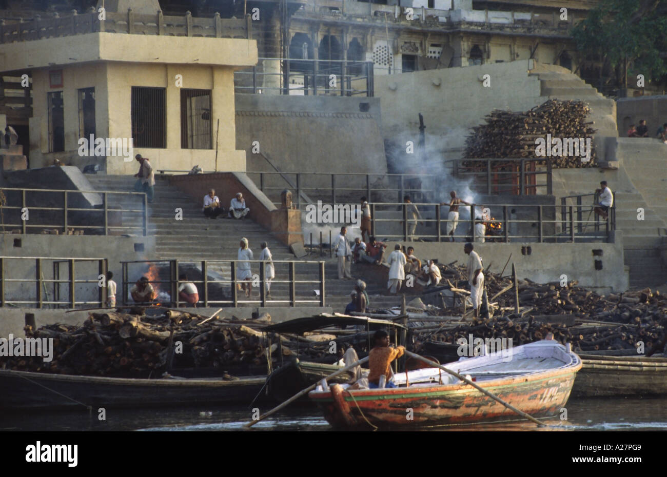 Man rowing boat by funeral pyres on ghats on banks of the sacred river