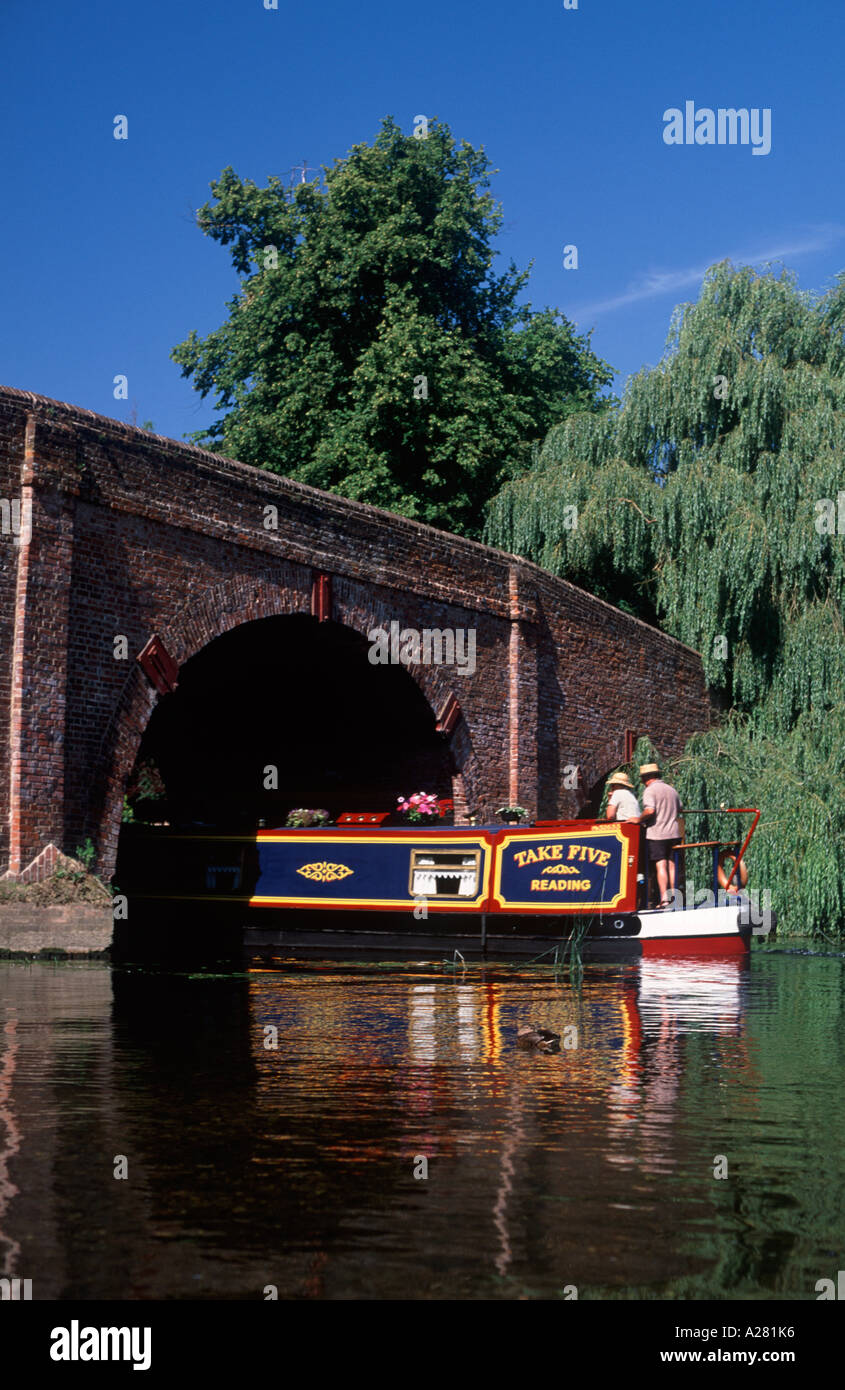 Couple steering traditional narrowboat beneath Sonning Bridge on the River Thames, Sonning, Berkshire, England Stock Photo