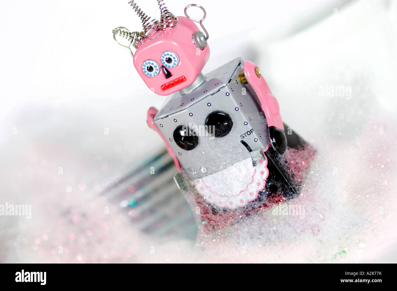 Female tin toy robot standing in front of dishes and covered in soap suds or washing up liquid bubbles Stock Photo