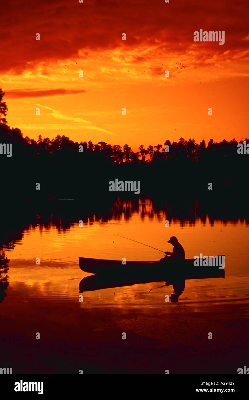 Silhouette of man fishing from canoe at sunset Stock Photo 
