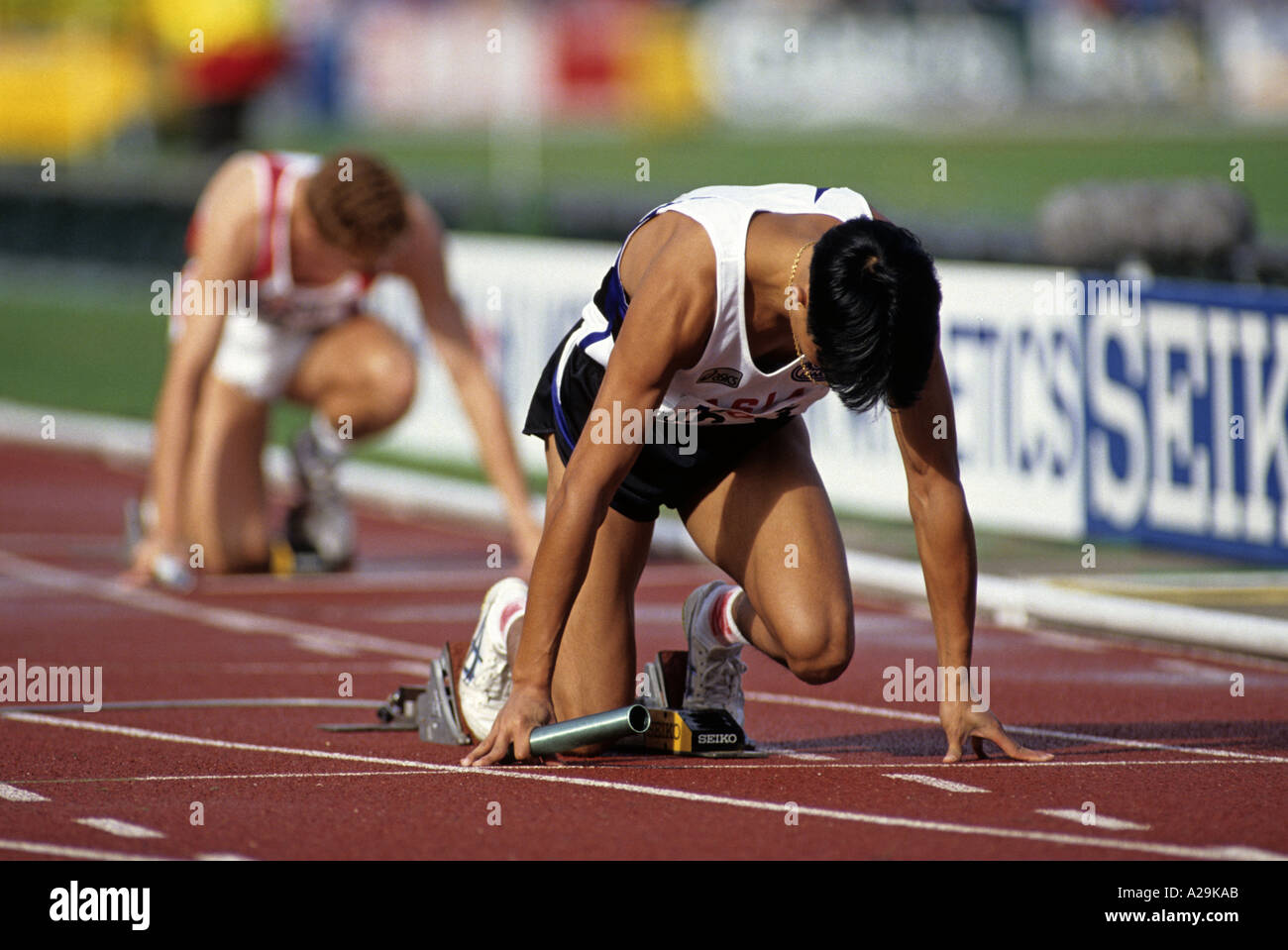 Two male relay runners on their starting blocks preparing themselves