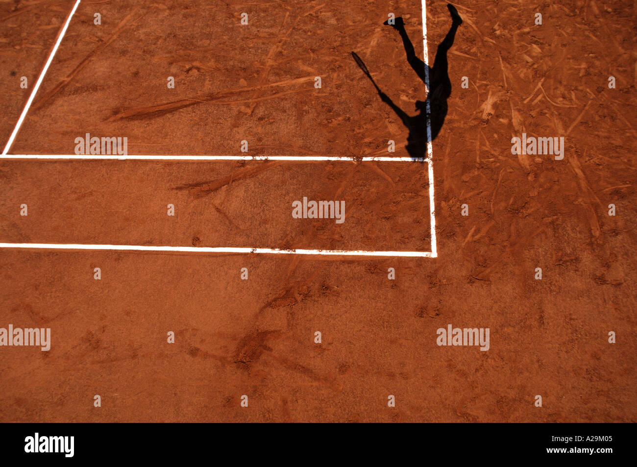 The shadow of a tennis player serving during a game on a clay court Stock Photo