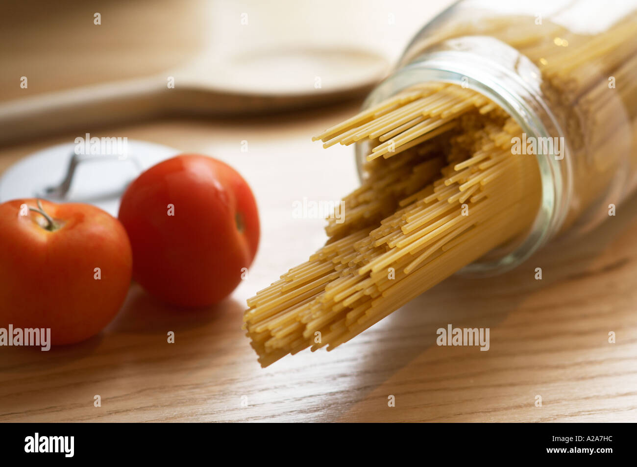 uncooked spaghetti in glass jar with wooden spoonand tomatoes in background Stock Photo