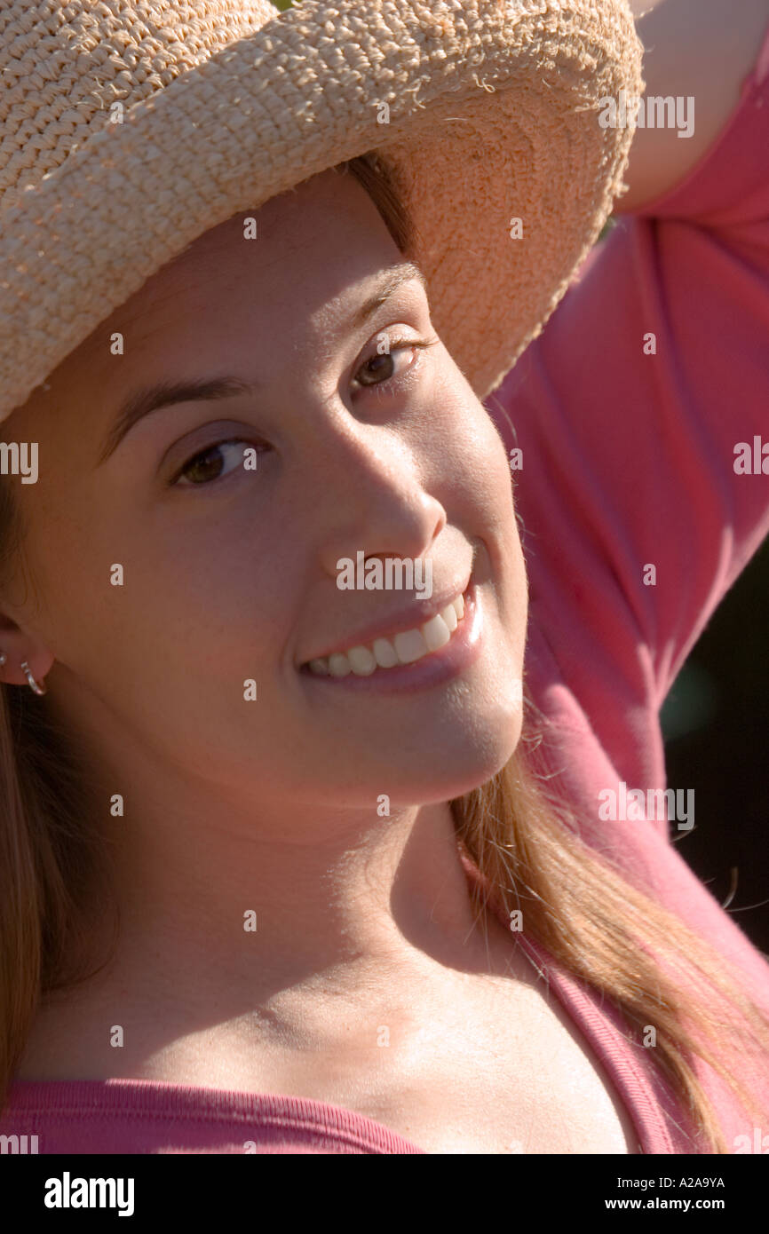 A smiling young Caucasian woman looks up with one hand holding her hat. Stock Photo