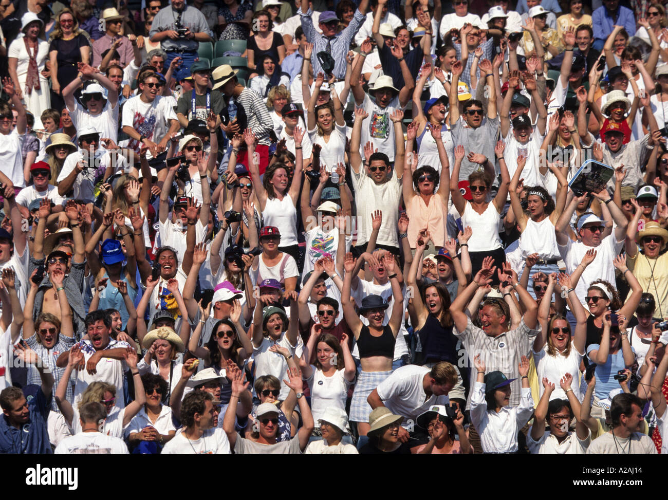 People in the crowd raise their arms in the air performing a Mexican Wave during a tennis match Stock Photo